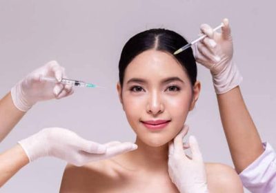 Mixed Asian young 20s woman going through skin care and aesthetic medical therapy and to be injected by hands of doctor with syringes in white background